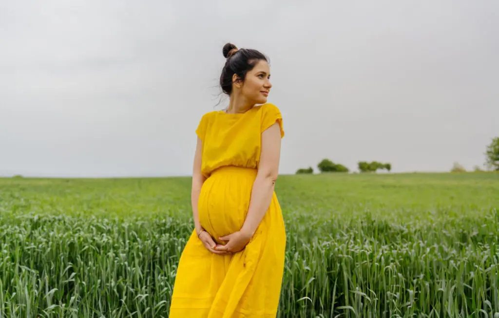 a pregnant woman in a yellow dress in a field of grass