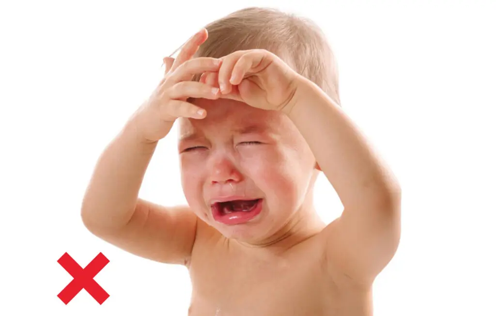 a baby crying with hands on forehead