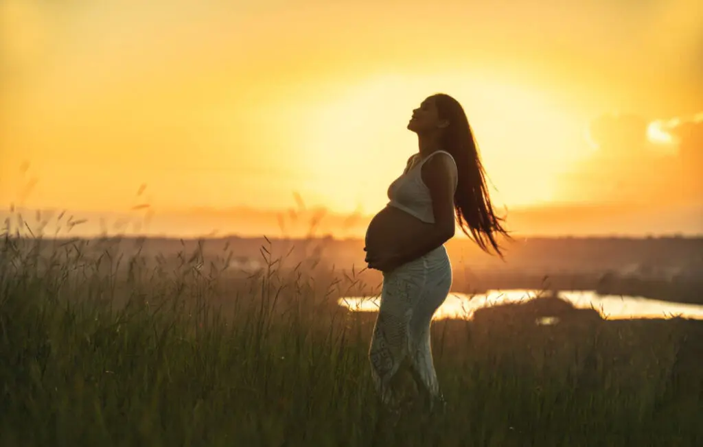 a pregnant woman standing in a field with her hands on her stomach