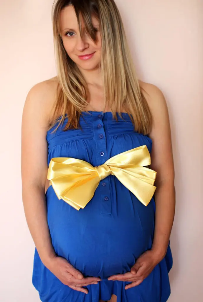 a pregnant woman wearing a blue dress with a yellow bow on her belly